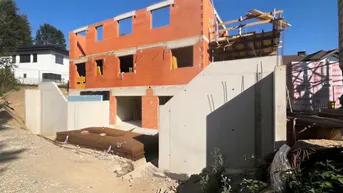 Neubau im Rohbau mit Ziegelwänden und Betonfundament unter blauem Himmel.