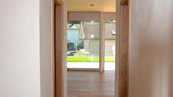 Heller Flur mit Holzboden und Holzdecke, der zu einem lichtdurchfluteten Raum mit Gartenblick führt.