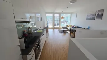 Heller, offener Wohn- und Essbereich mit moderner Küche, Holzboden und Zugang zum Balkon.