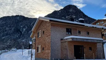 Modernes Holzhaus in verschneiter Berglandschaft unter bewölktem Himmel.