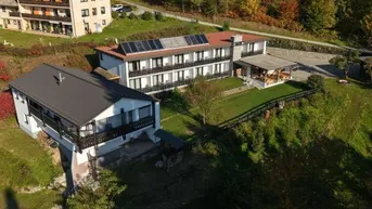 Luftaufnahme von mehreren Gebäuden in einer grünen Landschaft mit Solarpaneelen auf einem Dach.
