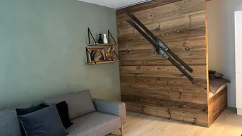 Gemütliches Wohnzimmer mit moderner Couch, Holzwand und alpiner Dekoration, die zum Entspannen einlädt.