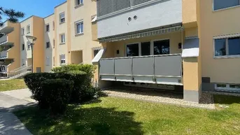 Mehrfamilienhaus mit gelber Fassade, Balkonen und grüner Umgebung unter blauem Himmel.