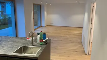 Heller, offener Wohnbereich mit moderner Kücheninsel und Holzboden, der zum Garten hin ausgerichtet ist.