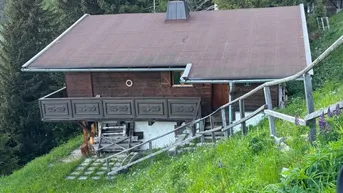 Rustikales Holzchalet auf einem grünen Hügel mit Balkon und umgebendem Wald.