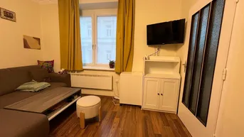 Gemütliches Wohnzimmer mit Sofa, Fernseher und Laminatboden, hell durch das Fenster.