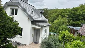 Modernes Einfamilienhaus mit grauem Dach und weißer Fassade, umgeben von viel Grün.