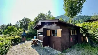 Rustikale Holzhütte mit kleiner gepflasterter Terrasse und Grillplatz im Grünen.