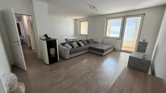 Helles Wohnzimmer mit modernem Pelletofen, gemütlichem Sofa und Zugang zum Balkon.