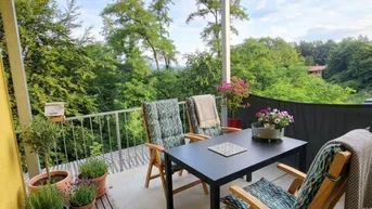 Gemütlicher Balkon mit Sitzgelegenheiten und vielen Pflanzen, umgeben von grüner Natur.