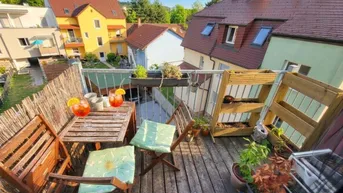 Gemütlicher Balkon mit Holzboden, Sitzgelegenheiten und Blick auf die umliegenden Häuser.