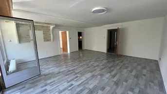 Geräumiges Wohnzimmer mit modernem Laminatboden, weiß gestrichenen Wänden und Zugang zum Balkon.