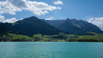 Idyllischer Blick auf einen See mit majestätischen Bergen im Hintergrund unter blauem Himmel.