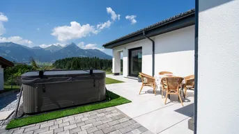 Große Terrasse mit Whirlpool und Sitzbereich, umgeben von einer beeindruckenden Berglandschaft.