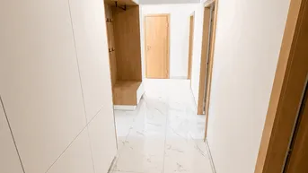 Heller Flur mit modernen weißen Fliesen in Marmoroptik und integrierter Garderobe.