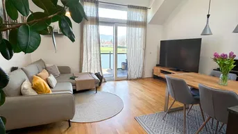 Helles Wohn-Esszimmer mit Holzboden, hohen Decken und Zugang zum Balkon.