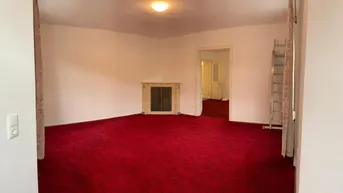 Geräumiges Wohnzimmer mit rotem Teppichboden und einem dekorativen Kamin in einem älteren Gebäude.