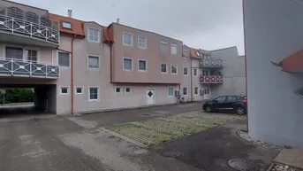 Mehrfamilienhaus mit mehreren Balkonen und einem Parkplatz im Freien unter bewölktem Himmel.