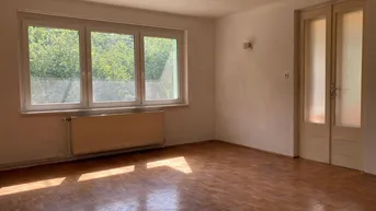 Helles Zimmer mit Parkettboden, großen Fenstern und Blick ins Grüne.