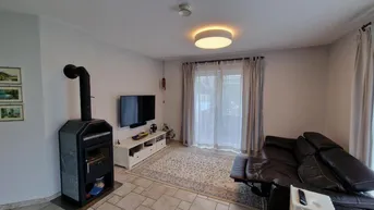 Gemütliches Wohnzimmer mit Kaminofen, Sofa und Zugang zur Terrasse.