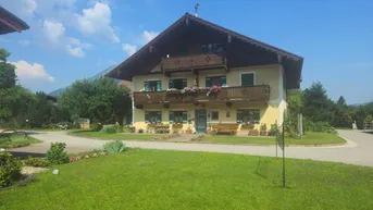 Traditionelles gelbes Haus mit grünen Fensterläden und Holzbalkonen, umgeben von einem gepflegten Rasen.