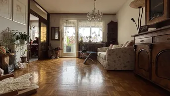 Helles Wohnzimmer mit Parkettboden, Kronleuchter und Zugang zu einem Balkon mit Ausblick.