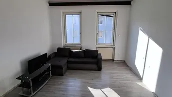 Helles Wohnzimmer mit Laminatboden, einem Sofa und Blick aus zwei Fenstern.
