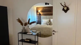 Schlafzimmer mit Holzwand, großem Spiegel und alpiner Dekoration, die sich im Spiegel widerspiegelt.