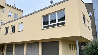 Modernes Gebäude mit heller Fassade und integrierten Garagen im Erdgeschoss.