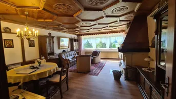Gemütlicher Wohn- und Essbereich mit kunstvoll geschnitzter Holzdecke und traditionellem Kamin.