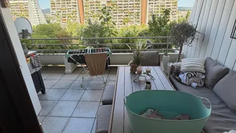 Geräumiger Balkon mit Sitzgelegenheiten, Markise und Blick auf die umliegenden Gebäude und Grünflächen.