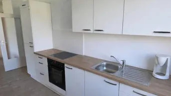 Moderne Einbauküche mit weißen Schränken, Holzarbeitsplatte und integrierten Geräten.