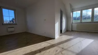 Helles, leeres Zimmer mit Holzboden und großen Fenstern, das viel Tageslicht hereinlässt.