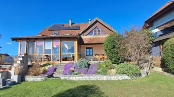 Charmantes Einfamilienhaus mit Wintergarten, Solaranlage und gepflegtem Vorgarten unter blauem Himmel.