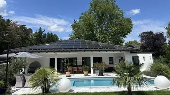 Modernes Einfamilienhaus mit Photovoltaikanlage, großem Pool und gepflegtem Garten unter blauem Himmel.