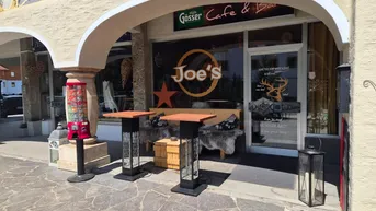 Außenansicht eines Cafés mit Sitzgelegenheiten unter einem Bogen und Blick auf die Straße.
