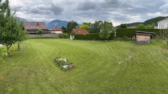Großes Gartengrundstück mit weitläufiger Rasenfläche, kleinem Schuppen und Bergblick unter bewölktem Himmel.
