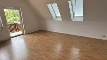 Heller Raum im Dachgeschoss mit Laminatboden, Dachfenstern und Zugang zu einem kleinen Balkon.