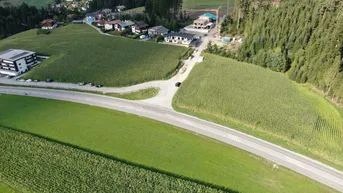 Luftaufnahme einer ländlichen Gegend mit Feldern, einer Straße und mehreren Gebäuden, umgeben von Natur.