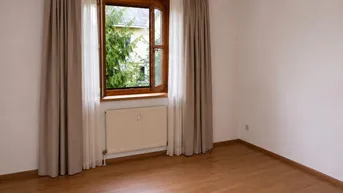 Helles Zimmer mit Laminatboden und Fenster mit Blick ins Grüne.