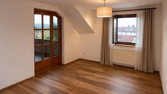 Helles Zimmer mit Laminatboden, Dachschräge und Zugang zu einem Balkon mit Aussicht.