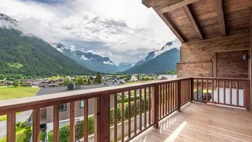 Geräumiger Balkon mit Holzboden und Geländer, bietet einen weiten Blick auf die umliegende Berglandschaft.