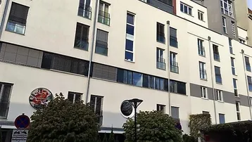 Moderne Wohnhausfassade mit vielen Fenstern und Balkonen in städtischer Umgebung.