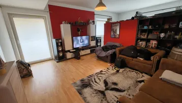 Geräumiges Wohnzimmer mit roter Akzentwand, Holzboden und Zugang zu einem Außenbereich.