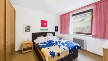 Gemütliches Schlafzimmer mit Blick ins Grüne, Holzkleiderschrank und Teppichboden.