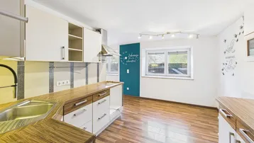 Helle Küche mit Holzarbeitsplatten, Laminatboden und einer auffälligen türkisfarbenen Akzentwand.