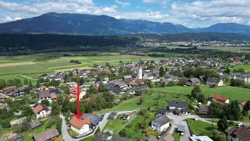 Weitläufige Luftaufnahme eines Dorfes mit Bergen im Hintergrund, das Objekt ist markiert.