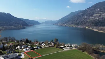 Luftaufnahme eines Baugrundstücks mit weitem Blick auf den See und die umliegende Berglandschaft.