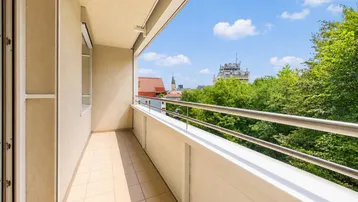 Langer Balkon mit Fliesenboden und Blick auf die Stadt und umliegende Bäume.