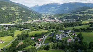 Umfassende Luftaufnahme einer Stadt in einem Tal, umgeben von grünen Hügeln und schneebedeckten Bergen.